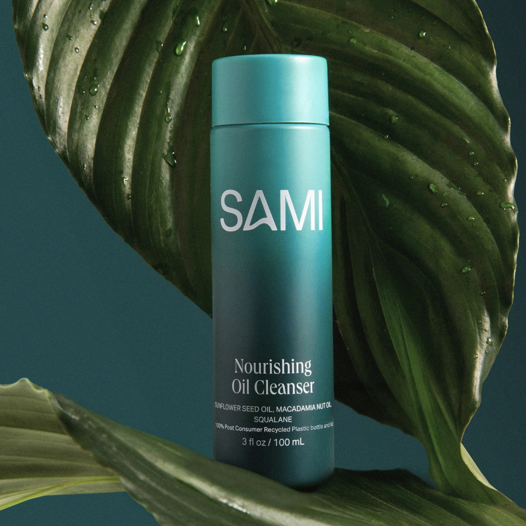 SAMI Nourishing Oil Cleanser in teal recyclable bottle surrounded by tropical leaves for gentle makeup removal