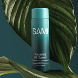 SAMI Nourishing Oil Cleanser in teal recyclable bottle surrounded by tropical leaves for gentle makeup removal