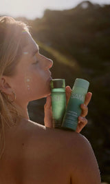 Woman holding SAMI Hydrating Cream Cleanser and Refining AHA + BHA Exfoliator no rinse skincare products, outdoors for gentle exfoliation and glowing beach-inspired beauty routine