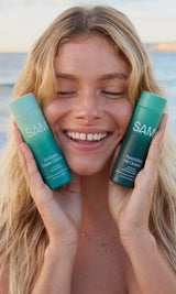 Woman holding SAMI Hydrating Cream Cleanser and Nourishing Oil Cleanser at the beach for glowing skin and effortless no-rinse cleansing routines