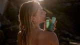 Woman holding SAMI Hydrating Cream Cleanser and Refining AHA + BHA Exfoliator outdoors, gentle exfoliation and glowing beach-inspired beauty routines